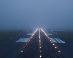 Airport shrouded in thick fog with approach lights barely visible, aircraft climbing away above fog layer after go-around