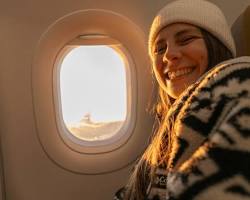 Relaxed passenger looking out airplane window at clouds below, peaceful expression, representing confidence in aviation safety